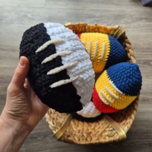 A hand holding a black and white crocheted football